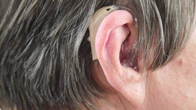Closeup senior woman with hearing aid in her ear. Health care, hear amplify, device for the deaf. 4K ProRes HQ codec