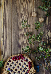 pie with berry filling on a brown wooden background with flowers, green leaves, walnuts, top view