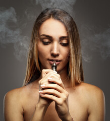 Beautiful woman is vaping. Dark background. Studio shooting.