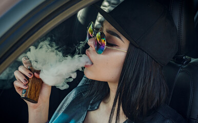 Young sexy woman is smoking (vaping) e-cigarette sitting in the car.