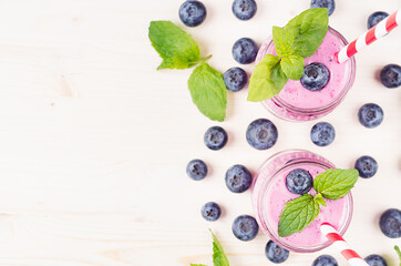 Naklejka na ściany i meble Decorative border of violet blueberry fruit smoothie in glass jars with straw, mint leaves, berries, close up, top view. White wooden board background, copy space.