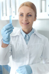 caucasian smiling chemist in uniform working in lab and looking at tube with reagent in chemical lab