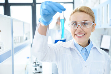 Smiling chemist in protective eyeglasses holding test tube with reagent in lab