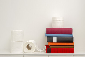 Read books in the bathroom, colorful books and toilet paper on the white tiled shelf