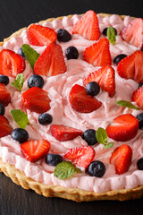 beautiful and tasty tart with strawberries and blueberries and a pink cream close-up. vertical