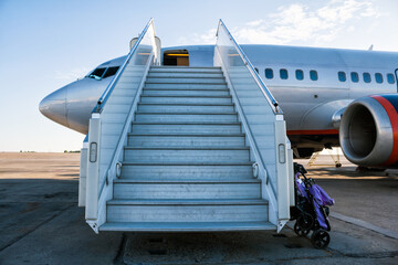 Airplane with a passenger boarding steps on the airport apron with a stroller prepared for the...