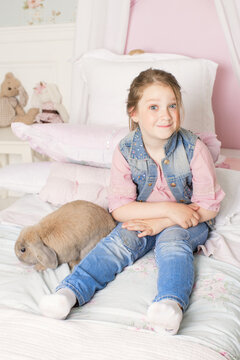 Little cute girl playing with a rabbit on the sofa at home. The way of life of the child. the concept of Pets