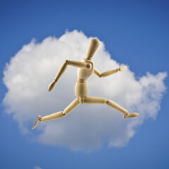 Wooden mannequin jumping or running. White cloud and blue sky as background.