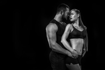 sensual sportive couple wearing sportswear, hugging and looking at each other isolated on black, black and white