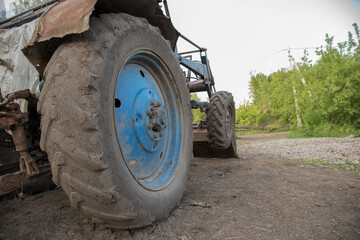 Fototapeta na wymiar Details of a blue village tractor with dirty wheels, engine, rudder and bucket with an arrow in the summer