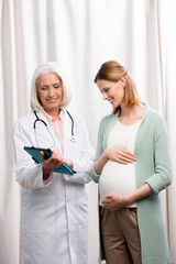 doctor showing results of examination to young pregnant woman on digital tablet