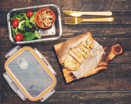 Preparing takeaway meal for children. School lunch box with salad, fried chicken and nuts on rustic wooden background. Healthy eating habits concept.