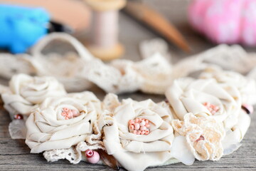 Mixed materials flower necklace, glue hot gun, scissors, thread, needle, felt on vintage wooden table. Summer fashion fabric jewelry for women and girls. Idea of recycling fabric into elegant necklace
