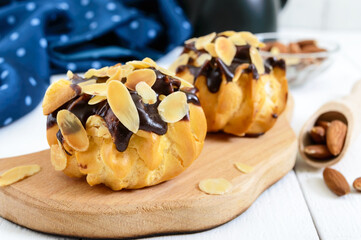 Eclairs, covered with dark chocolate and almond flakes decoration on a white wooden background.
