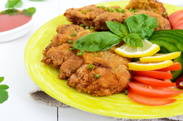 Schnitzel with vegetables, tomato sauce on a white wooden background. Close up