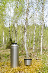 Thermos with beverages in a bright forest