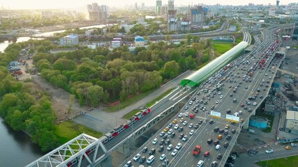 Aerial shot of heavy traffic jam and moving commuter trains in the rush hour. Private cars versus public transport concept