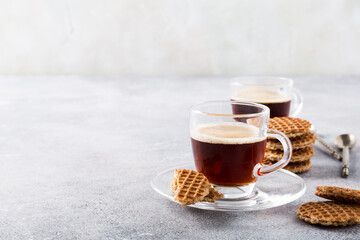 Glass cups of coffee with mini stroopwafel, syrupwaffles cookies on light gray background with copy space.