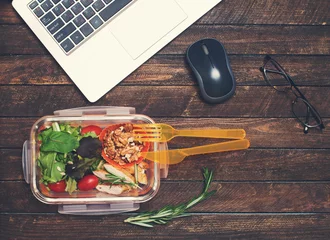 Fotobehang Gezonde zakenlunch op de werkplek. Groenten en gebakken kip lunchbox op bureau met laptop en bril. © Polina Ponomareva