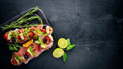 Bruschetta with meat, olives, herbs and parmesan cheese on bread. Cold snacks. Italian cuisine. On Wooden background.