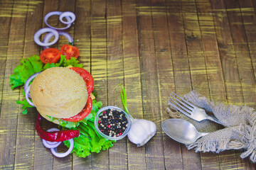 Hamburger with cheese, meat, tomatoes and onions and herbs. On Wooden background. Top view. Free space.