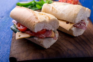 Sandwich with jamon, arugula, tomatoes, cheese on wooden board blue background. Rustic. Two.