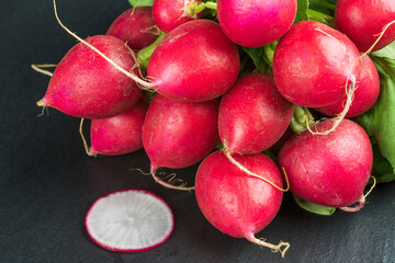 Bundle and a single slice of radish on black stone slab.