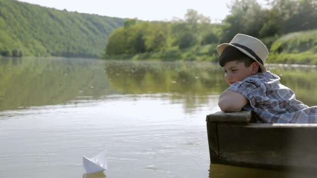 The boy puts a paper boat on the water and let the sail