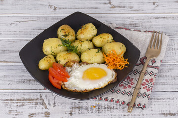 Boiled young potatoes with fried eggs, carrot and tomato. Close up