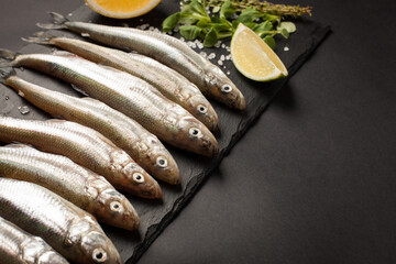 Fresh sea fish smelt or sardines ready for cooking with lemon, thyme, and coarse sea salt on a blue background. The concept of fresh, healthy seafood. Top view with copy space.