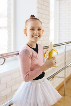 Girl ballerina eating a banana in ballet class
