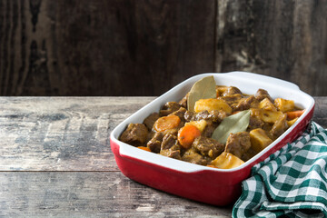 Beef meat stewed with potatoes, carrots and spices in ceramic pot on wooden table
