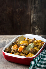 Beef meat stewed with potatoes, carrots and spices in ceramic pot on wooden table
