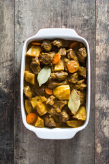 Beef meat stewed with potatoes, carrots and spices in ceramic pot on wooden table
