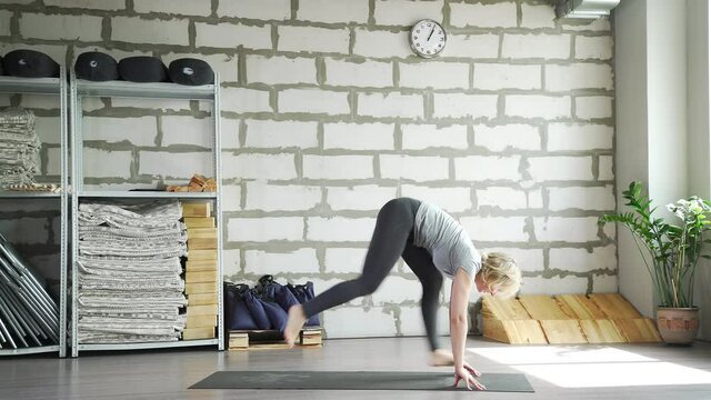 Middle-aged woman does yoga in a bright space with a brick wall and does stretching. The woman folded her hands in the lock behind her back and leaned forward. Endurance, flexibility. Practice of yoga