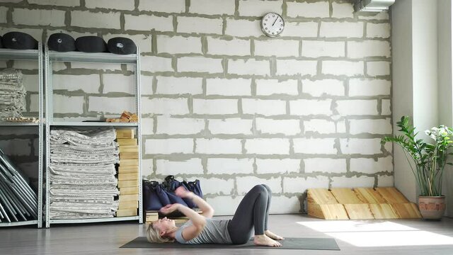 Middle-aged woman does yoga in a bright space with a brick wall and does stretching. Mature woman practices yoga and does a bridge exercise. Ardha chakrasana