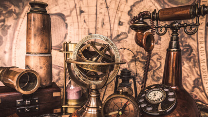 Fototapeta na wymiar Antique sundial compass, compass, telescope, vintage telephone and wooden chest box on ancient world map.