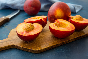 Ripe juicy nectarines, whole and halved on wood cutting board, knife, blue kitchen towel, modern...