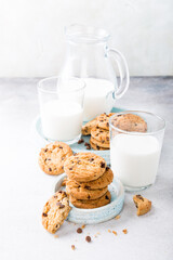 Stack of chocolate chip cookies on blue stone plate with glass of milk on light gray background. Selective focus. Copy space.
