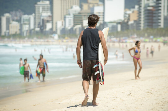 Scenic afternoon view of Ipanema Beach in Rio de Janeiro, Brazil with an unrecognizable surfer walking on a bright day with the city skyline in the distance