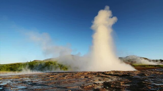 Eruption of geyser in Iceland. Winter cold colors, sun lighting through the steam
