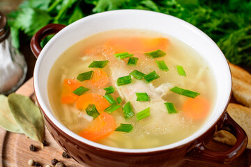 Homemade chicken soup with noodles and vegetables in ceramic bowl on wooden table.