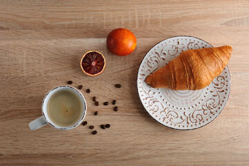 croissant on a plate with a Cup of coffee and red blood orange