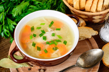 Homemade chicken soup with noodles and vegetables in ceramic bowl on wooden table.