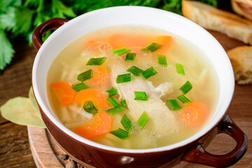 Homemade chicken soup with noodles and vegetables in ceramic bowl on wooden table.