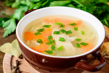 Homemade chicken soup with noodles and vegetables in ceramic bowl on wooden table.