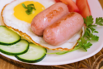Breakfast of fried mini sausages with vegetables and eggs on a white plate close-up