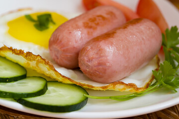 Breakfast of fried mini sausages with vegetables and eggs on a white plate close-up