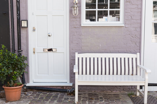 Puerta de madera blanca con fachada lila y banco de madera.