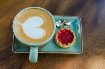 coffee cup with heart shape with strawberry biscuit on blue plate